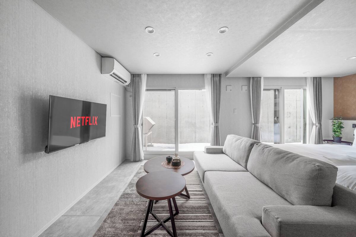 Ein modernes Hotelzimmer mit Flachbildfernseher, einer Couch, einem kleinen Couchtisch und einer Schiebeglastür zum Balkon.