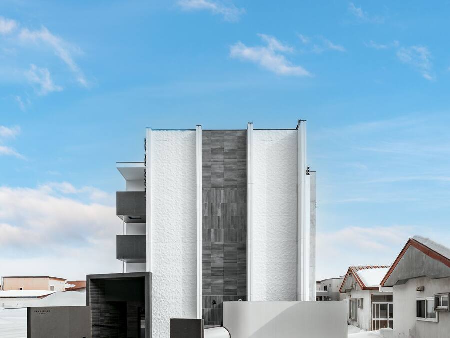 Un edificio moderno con fachada blanca, un elemento vertical central y un estacionamiento cubierto de nieve.