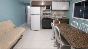 Eine kleine Küche mit Kühlschrank, Mikrowelle, Herd und Essecke mit Stühlen.