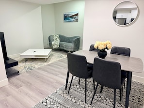 A modern living room with a dining area, a sofa, a coffee table, and a painting on the wall.