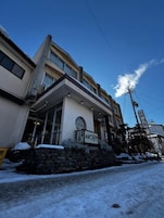 A hotel with a stone facade, a sign with Japanese characters, and a clear blue sky.
