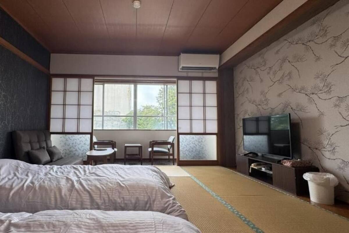 A traditional Japanese-style room with tatami flooring, a futon bed, a television, and a sliding door.