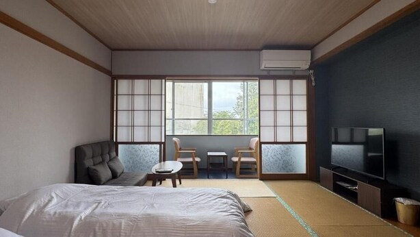 A room with tatami flooring, a bed, a TV, and a view through large windows. - turuyaryokan (Yamanouchi)
