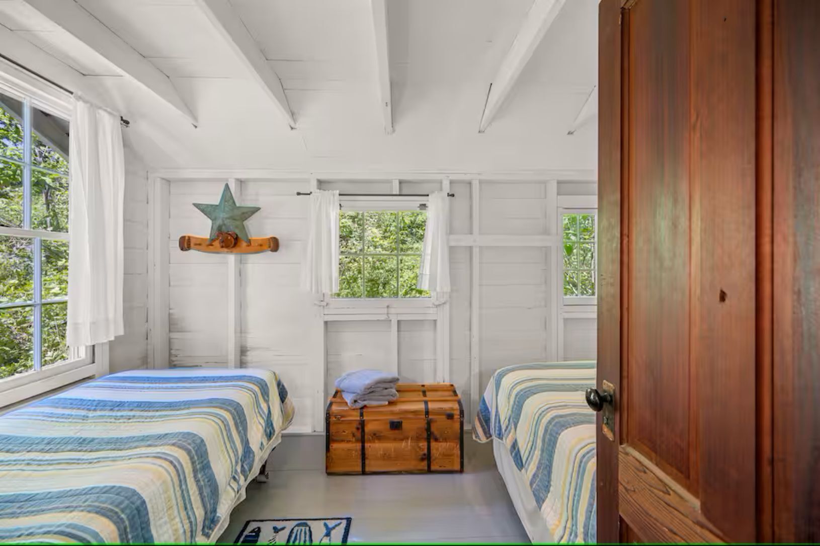A room with two beds, a star decoration, a window, and a wooden chest.