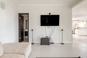 A modern living room with a flat-screen TV mounted on the wall, a sofa, and a small table with electronic devices. - Penthouse By The Sea (Montego Bay)
