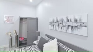 Et moderne soveværelse med en seng, et sengebord, en lampe, en dør, et indrammet billede og et bykunstværk på væggen.