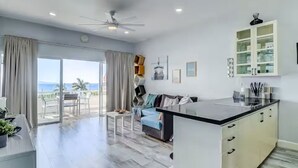 Et moderne køkken med en central ø, et spiseområde med bord og stole, og en stor skydedør, der fører til en balkon med udsigt.
