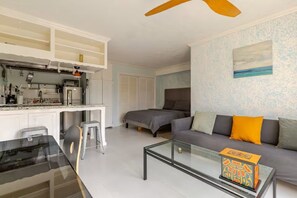 Ein kompakter Wohnraum mit Küchenzeile, einer Couch, einem Glastisch und einem Deckenventilator.