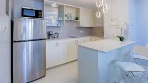 Eine moderne Küche mit einem Edelstahl-Kühlschrank, weißen Schränken, einer Mikrowelle und einer Bar mit weißen Stühlen.