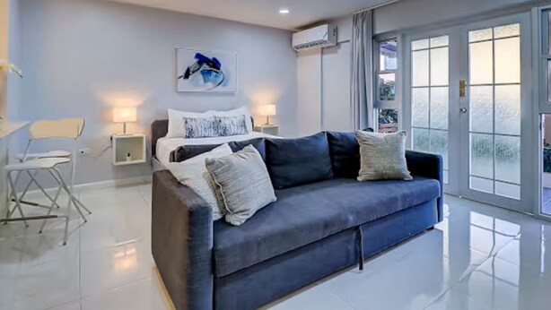Ein modernes Wohnzimmer mit einem dunkelblauen Sofa, einem weißen Sessel, einem Bild an der Wand und einem großen Fenster mit Aussicht.