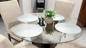 Una mesa redonda de cristal con cuatro sillas, una planta pequeña y un dispensador de agua al fondo.
