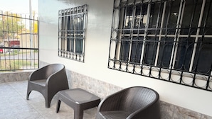 Un patio con dos sillas de mimbre, una mesita, un portón metálico y una ventana con reja.