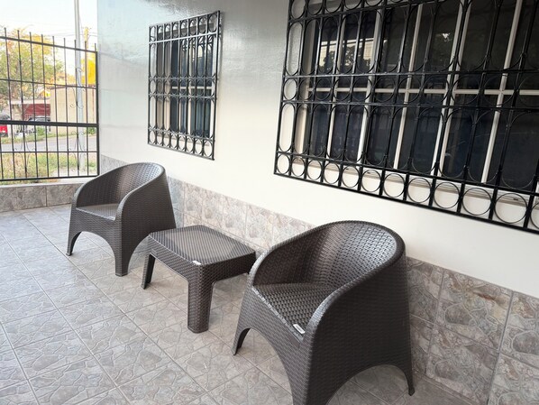 A patio area with two wicker chairs and a small table, a metal gate, and a window with a metal grille.