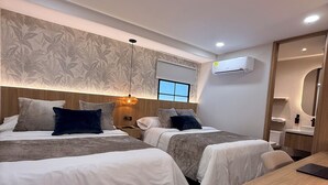 Habitación de hotel moderna con dos camas, un cabecero de madera, una mesita y una ventana con persianas.