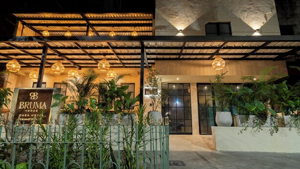 Entrada de hotel con un letrero, un patio cubierto y plantas en macetas.