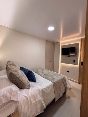 Une chambre à coucher avec un lit, des oreillers, un téléviseur fixé au mur et une porte.