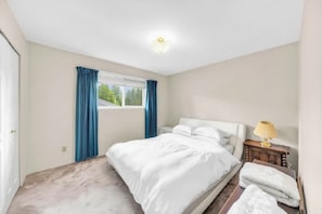 Een slaapkamer met een bed, nachtkastje, lamp en raam met gordijnen.