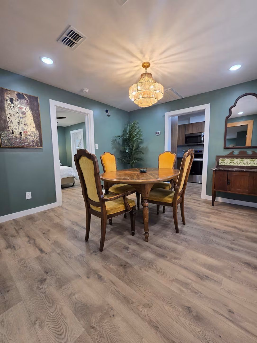 Une salle à manger avec une table et des chaises en bois, un lustre et un tableau au mur.
