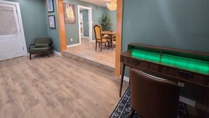 Um quarto com piso de madeira, parede verde, área de jantar com mesa e cadeiras, e um banco com luz verde.