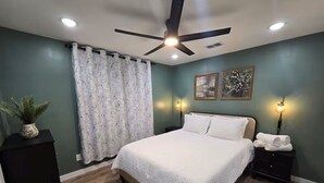 Quarto com cama, ventoinha no teto, luminárias na parede e planta em vaso.