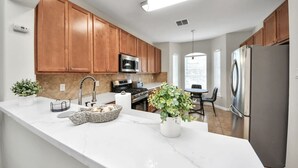 Una cocina moderna con armarios de madera, un refrigerador de acero inoxidable y un comedor con mesa y sillas.