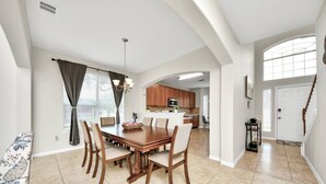 Un área de comedor con una mesa y sillas de madera, una cocina al fondo y una escalera que sube a otro piso.
