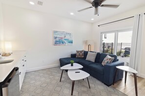 Ein modernes Wohnzimmer mit einer Couch, zwei Beistelltischen, einem Deckenventilator und einem Bild an der Wand.