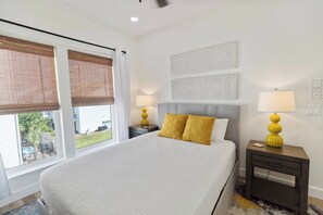 Ein Hotelzimmer mit einem großen Bett, zwei Nachttischen, einem Fenster mit Jalousien und Blick ins Freie.