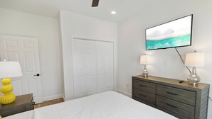 Ein Schlafzimmer mit einem Bett, einem Schminktisch, zwei Lampen, einem an der Wand befestigten Fernseher und einer Tür.