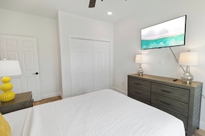 Ein Schlafzimmer mit einem Bett, einem Schminktisch, zwei Lampen, einem an der Wand befestigten Fernseher und einer Tür.