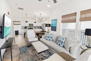 A modern living room with a sofa, a coffee table, a TV, and a kitchen in the background. - 🌊 Villas Laguna Beach #4 –  Gulf Views, Pool, Pets OK, Beach Access (Panama City Beach)