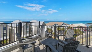 A balcony with Adirondack chairs and a table, overlooking a beach and buildings. - 🌊 Villas Laguna Beach #4 –  Gulf Views, Pool, Pets OK, Beach Access (Panama City Beach)