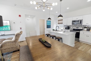 A modern kitchen with white cabinets, a central island, and a dining area with a wooden table and wicker chairs. - 🌊 Villas Laguna Beach #4 –  Gulf Views, Pool, Pets OK, Beach Access (Panama City Beach)