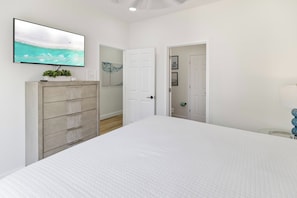 A bedroom with a bed, a TV on the wall, a door leading to a bathroom, and a hallway. - 🌊 Villas Laguna Beach #4 –  Gulf Views, Pool, Pets OK, Beach Access (Panama City Beach)