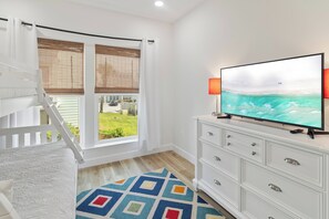 A room with a television on a white cabinet, a staircase, and a view of the outdoors. - 🌊 Villas Laguna Beach #4 –  Gulf Views, Pool, Pets OK, Beach Access (Panama City Beach)