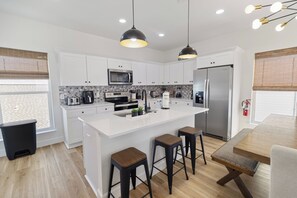 A modern kitchen with white cabinets, a central island with stools, stainless steel appliances, and pendant lighting. - 🌊 Villas Laguna Beach #4 –  Gulf Views, Pool, Pets OK, Beach Access (Panama City Beach)