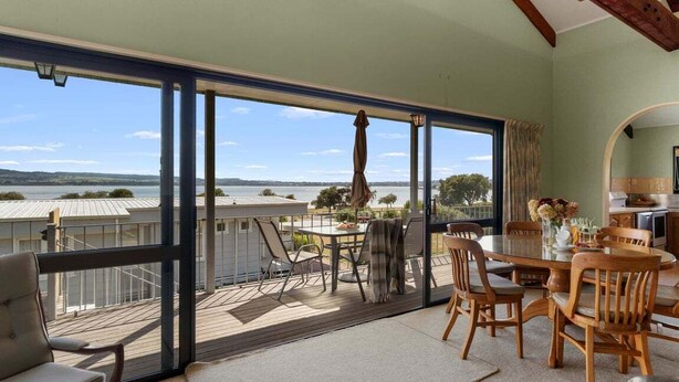 Een balkon met uitzicht op het water, een eethoek met houten meubels, en een groot raam.