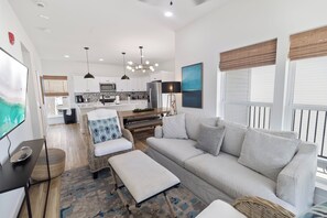 Ein modernes Wohnzimmer mit einer Couch, Hocker und einem Essbereich mit Tisch und Stühlen.