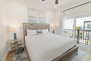 A bedroom with a large bed, two bedside lamps, a glass side table, a wooden headboard, and a view of the outside through a sliding door. - 🌊 Villas Laguna Beach #5 - Pool, Rooftop Terrace, Pets OK!, Walk to Beach (Panama City Beach)
