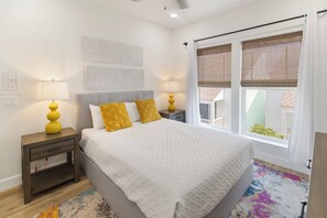 Ein Schlafzimmer mit einem Bett, zwei Nachttischen, einer Lampe, einem Fenster mit Jalousien und einer Wand mit strukturierter Dekoration.