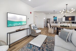 Ein modernes Wohnzimmer mit einem großen Flachbildfernseher, einem Essbereich mit Holztisch und einer Küche mit einem modernen Herd.