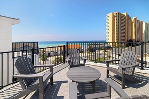 A balcony with outdoor furniture, a view of the ocean, and high-rise buildings in the background. - Villas of Laguna Beach #7 - Gulf Views. Pets Ok! Rooftop Terrace. Walk to Beach (Panama City Beach)