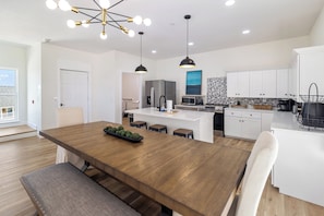 A modern kitchen with white cabinets, a central island, and a dining area with a wooden table. - Villas of Laguna Beach #7 - Gulf Views. Pets Ok! Rooftop Terrace. Walk to Beach (Panama City Beach)