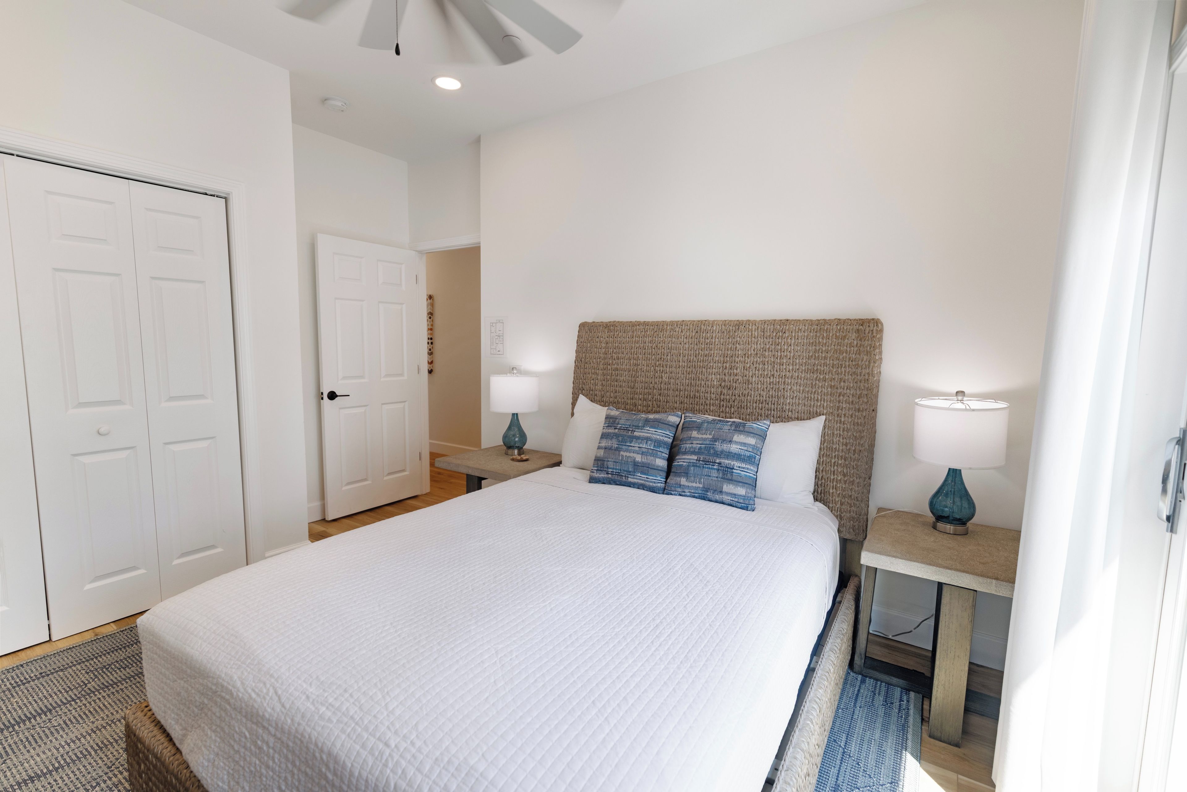 A bedroom with a large bed, two bedside tables with lamps, a door, and a ceiling fan.