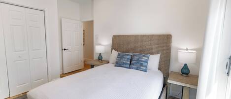 A bedroom with a large bed, two bedside tables with lamps, a door, and a ceiling fan.