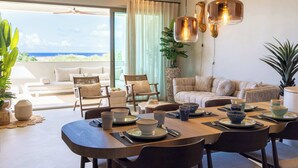 A modern dining area with a table set for four, a sofa, and a view of the ocean. - Florijn 7 | Ocean View Penthouse at The Reef (Willemstad)