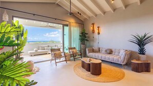 A spacious living room with a large window, a sofa, chairs, a coffee table, and various plants. - Florijn 7 | Ocean View Penthouse at The Reef (Willemstad)