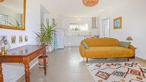 Ein modernes Wohnzimmer mit einer Couch, einem Esstisch, einem großen Spiegel und einer Küche im Hintergrund.