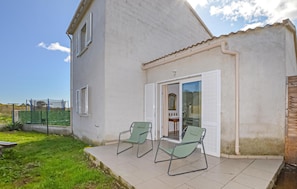 Uma casa com varanda, duas cadeiras, porta de correr e um pequeno jardim.