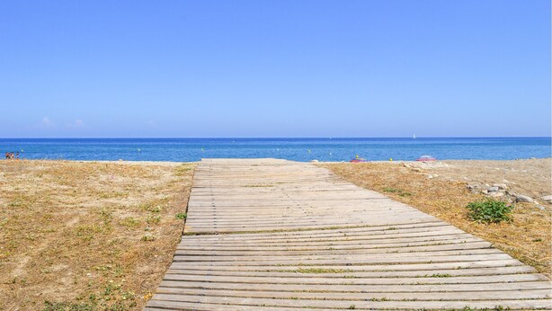 Ein hölzerner Steg führt zu einem Strand unter blauem Himmel.
